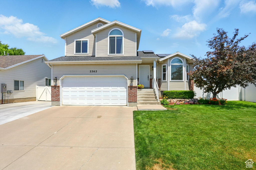 View of front facade with roof mounted solar panels, a garage, driveway, brick siding, and a gate