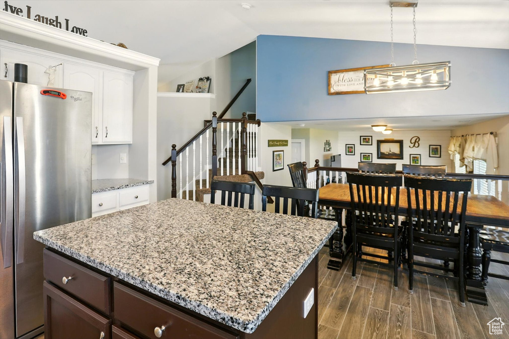 Kitchen featuring freestanding refrigerator, vaulted ceiling, white cabinetry, dark wood finished floors, and light stone counters