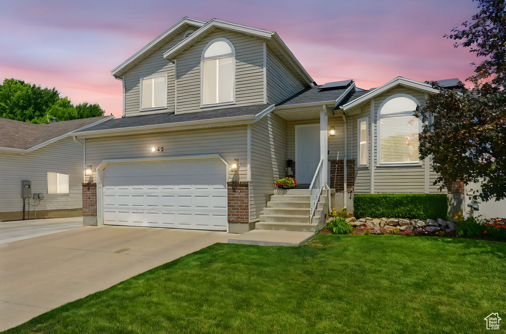 Split level home featuring a garage, solar panels, a front yard, and concrete driveway