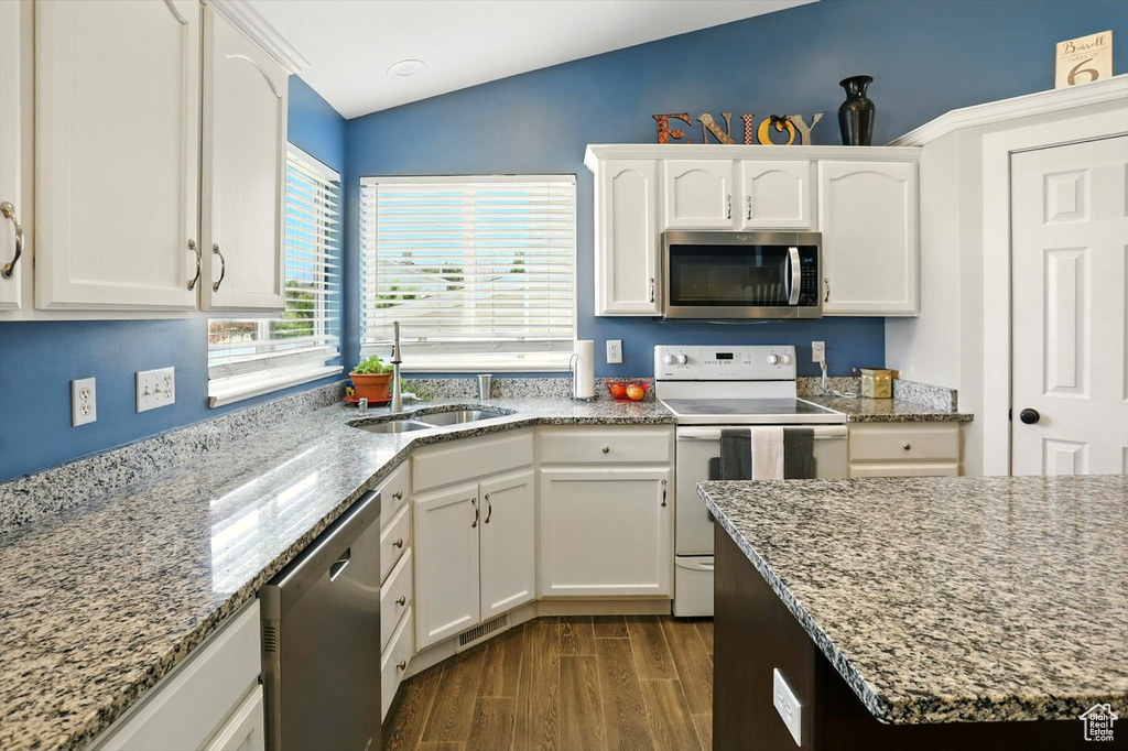 Kitchen with appliances with stainless steel finishes, vaulted ceiling, white cabinetry, dark wood-style flooring, and light stone counters