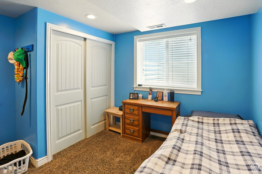 Bedroom with dark carpet, a closet, a textured ceiling, and recessed lighting