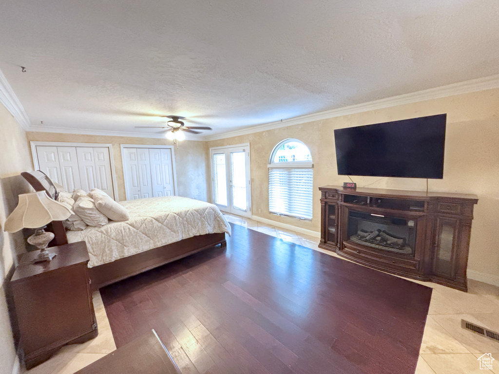 Bedroom featuring multiple closets, crown molding, a textured ceiling, wood finished floors, and ceiling fan