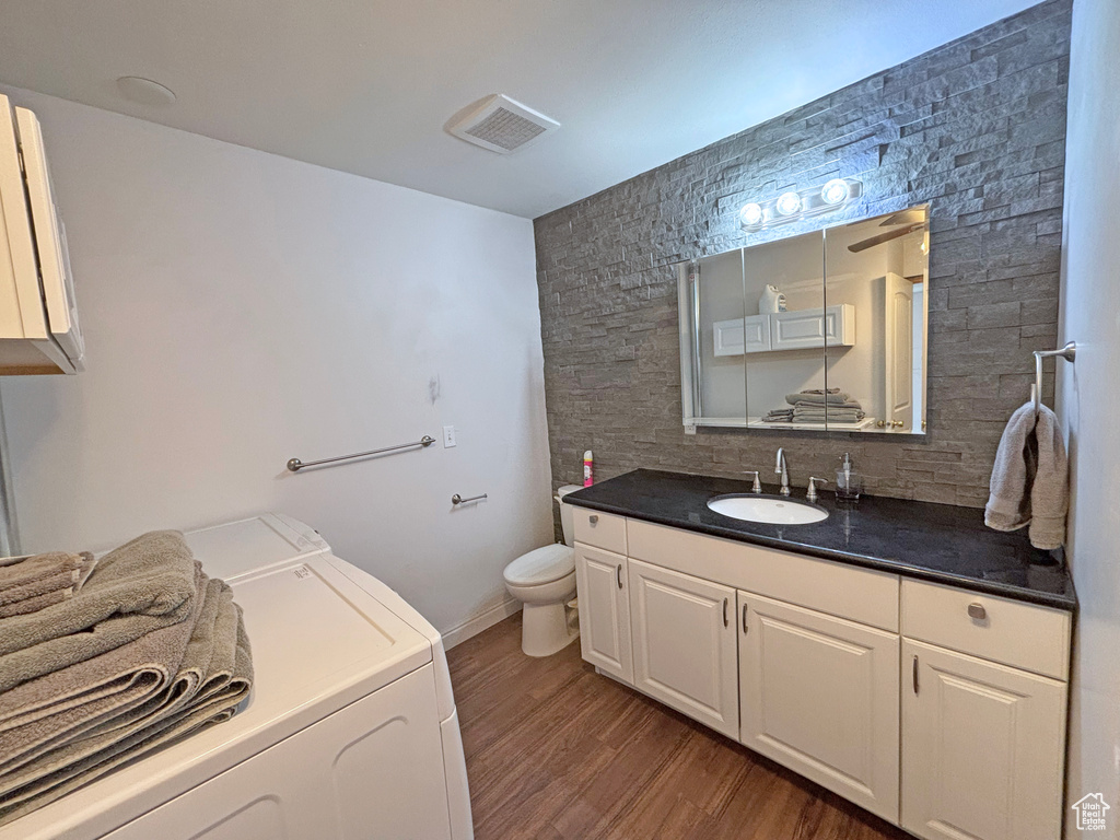 Bathroom featuring washer and dryer, vanity, wood finished floors, and decorative backsplash