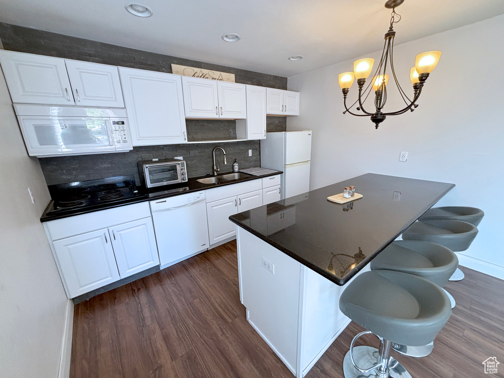 Kitchen with white appliances, a kitchen breakfast bar, dark wood-type flooring, tasteful backsplash, and recessed lighting