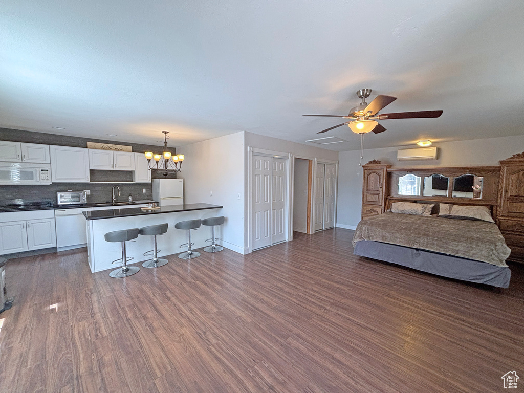 Kitchen with white appliances, dark countertops, a breakfast bar area, open floor plan, and white cabinets