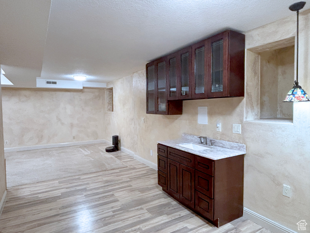 Kitchen featuring light wood-type flooring, light countertops, glass insert cabinets, and dark brown cabinets