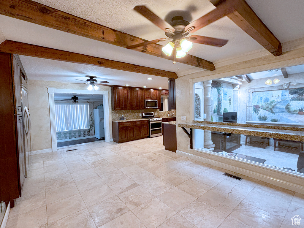 Kitchen with appliances with stainless steel finishes, a ceiling fan, beam ceiling, light countertops, and decorative backsplash