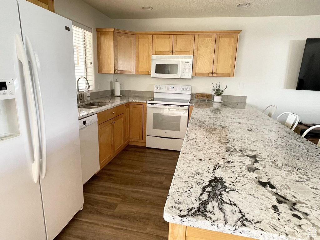 Kitchen with white appliances, dark wood finished floors, light stone countertops, and a peninsula