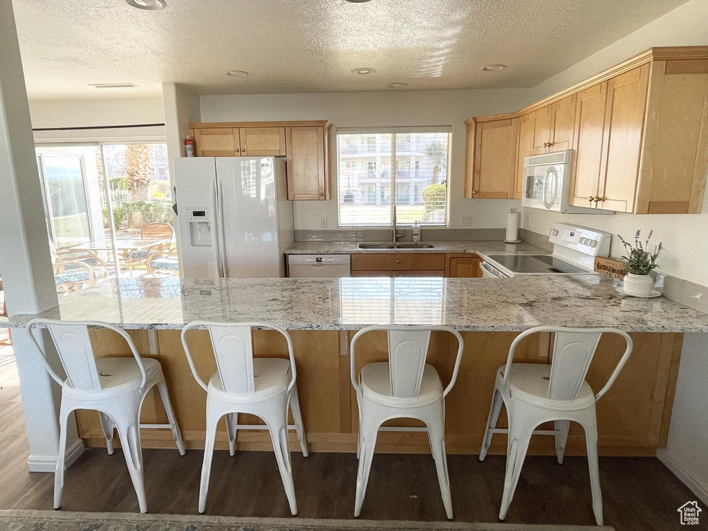 Kitchen with white appliances, a textured ceiling, a peninsula, light stone countertops, and wood finished floors