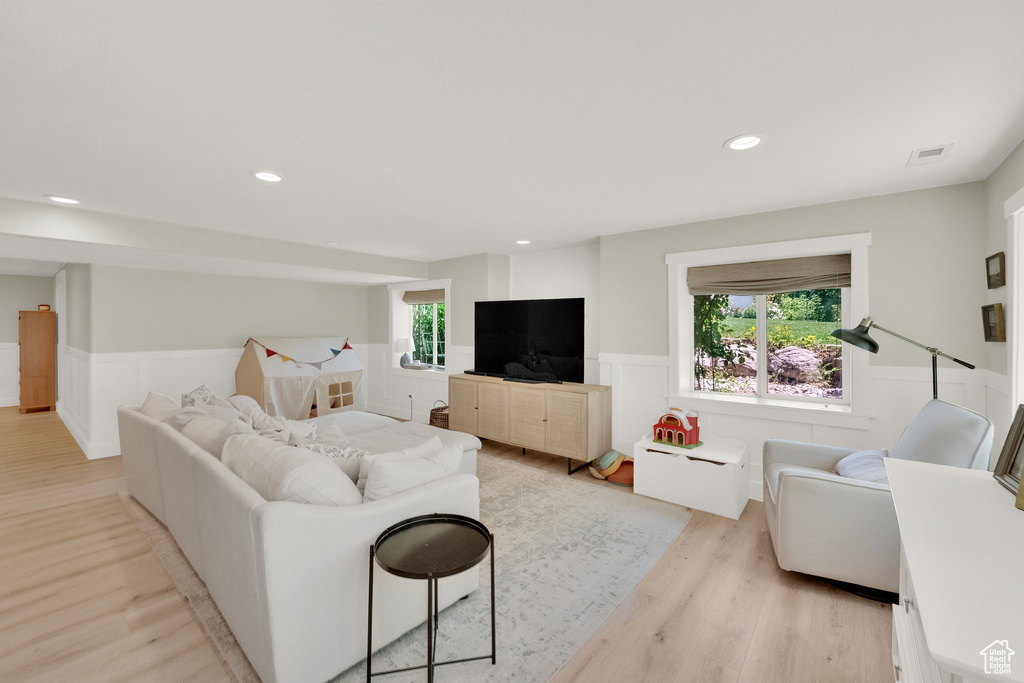 Living area with wainscoting, light wood-style floors, healthy amount of natural light, and recessed lighting