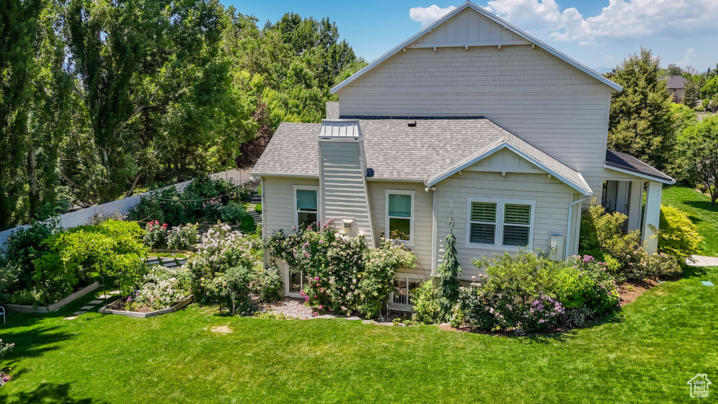Back of house featuring a garden, a shingled roof, and a lawn
