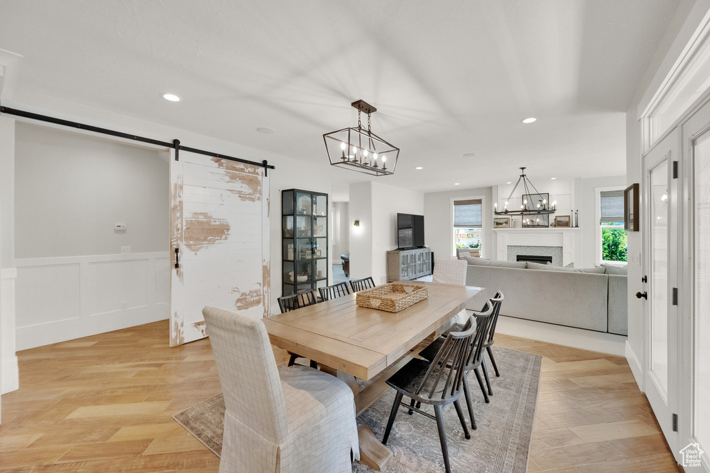 Dining space with a barn door, a fireplace, a chandelier, recessed lighting, and wainscoting