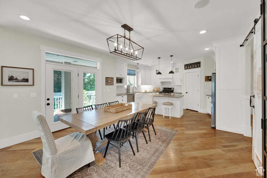 Dining area with recessed lighting, a barn door, light wood-type flooring, and a chandelier