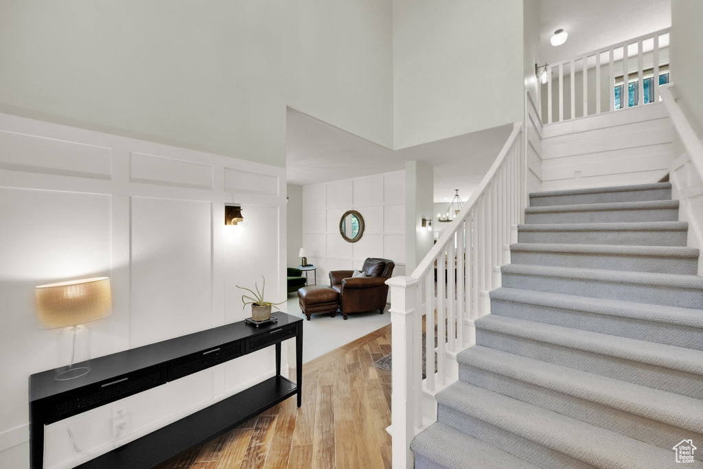 Staircase with wood finished floors, a decorative wall, a high ceiling, a chandelier, and a wainscoted wall