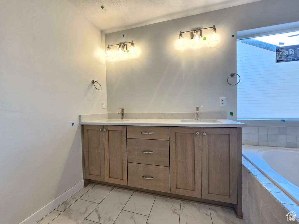 Bathroom with marble finish flooring, a relaxing tiled tub, and double vanity