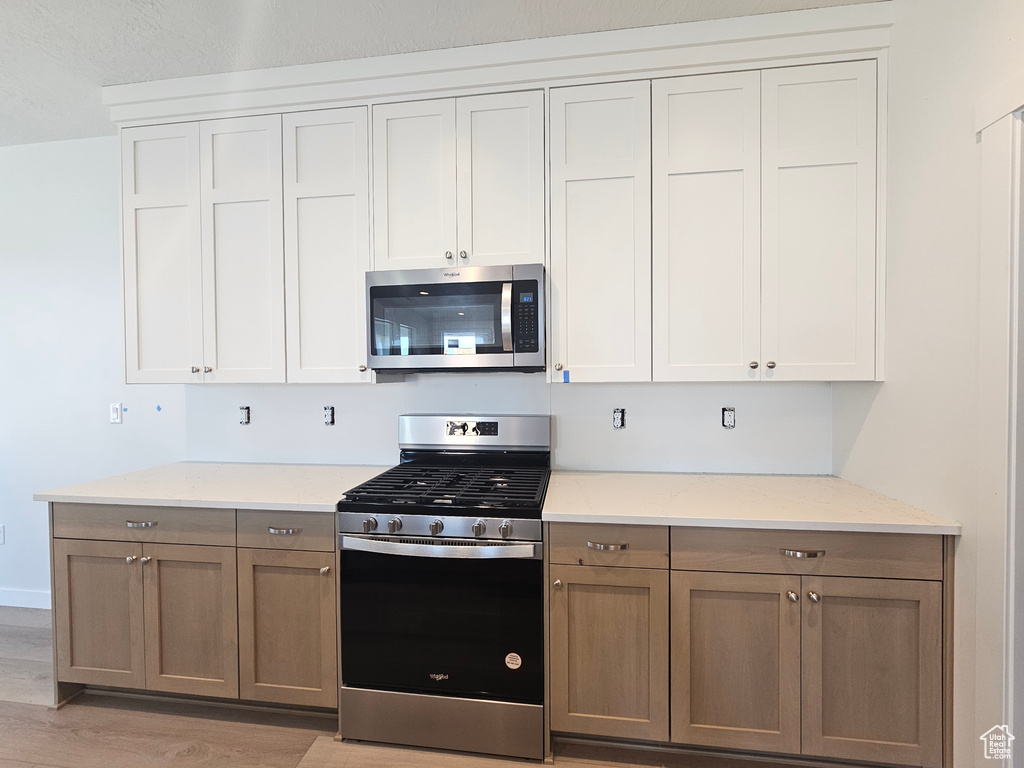 Kitchen featuring stainless steel appliances, light wood finished floors, and light stone counters
