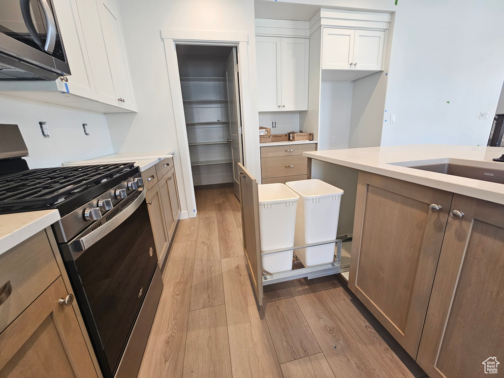 Kitchen with stainless steel appliances, light wood-type flooring, white cabinetry, and light countertops