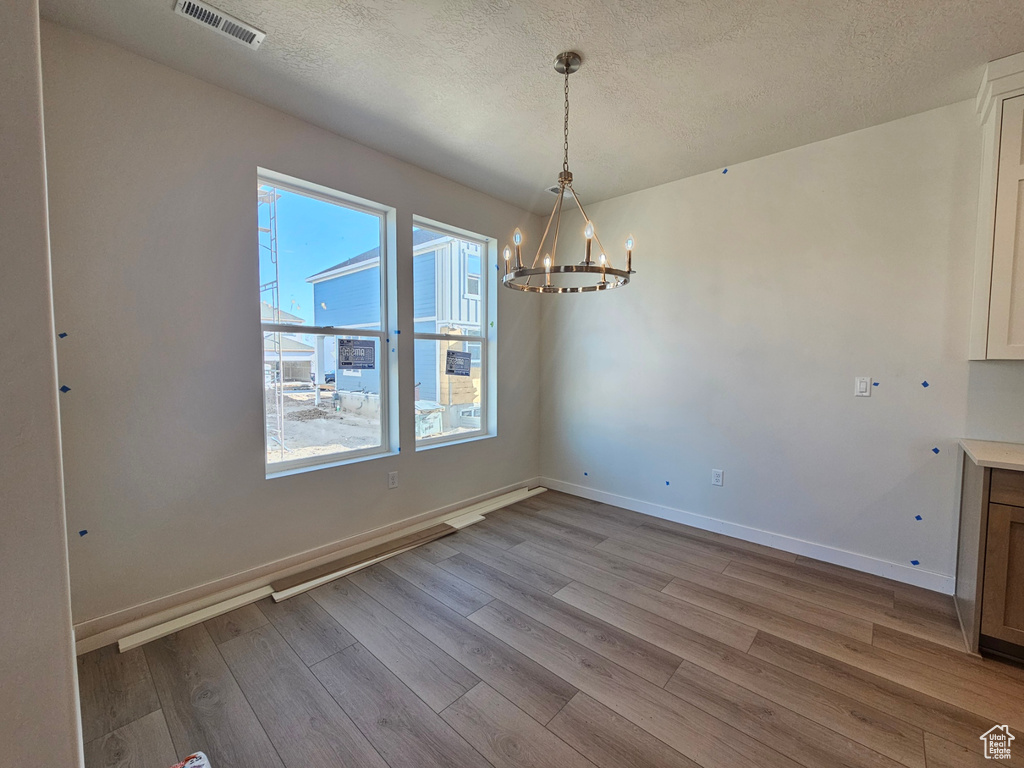 Unfurnished dining area featuring a chandelier, wood finished floors, and a textured ceiling