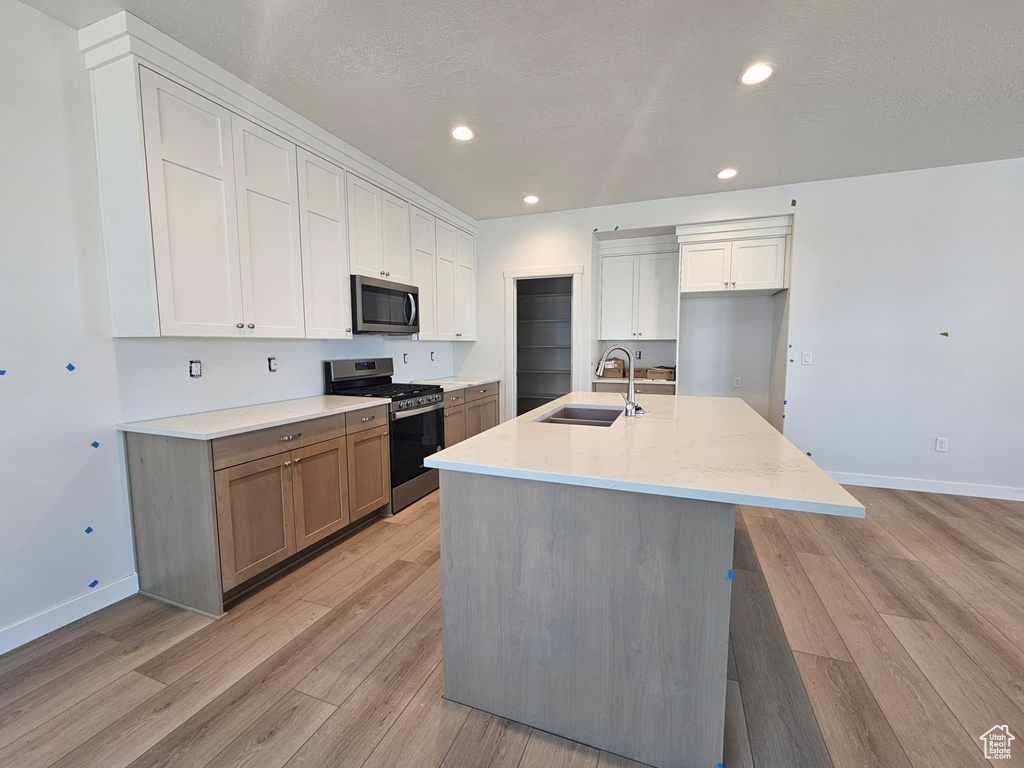 Kitchen with appliances with stainless steel finishes, light wood-style floors, white cabinets, an island with sink, and recessed lighting