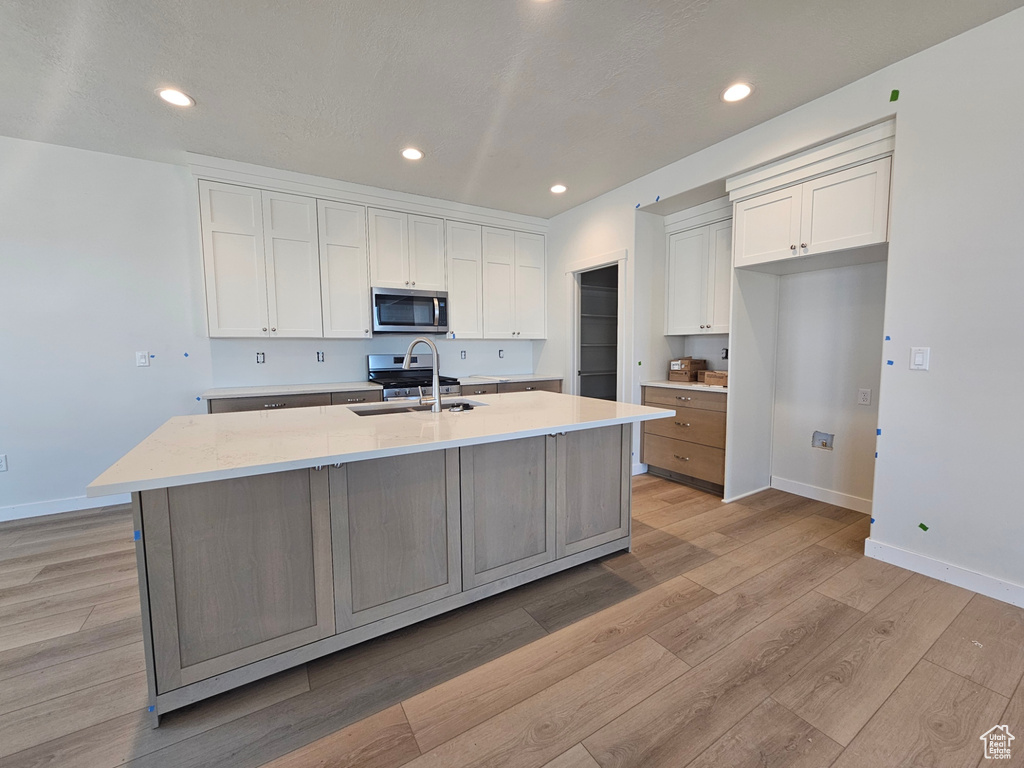 Kitchen featuring stainless steel appliances, white cabinets, a center island with sink, light wood-style flooring, and recessed lighting