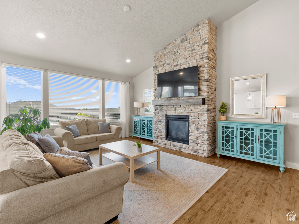 Living room with wood finished floors, a textured ceiling, a stone fireplace, high vaulted ceiling, and recessed lighting