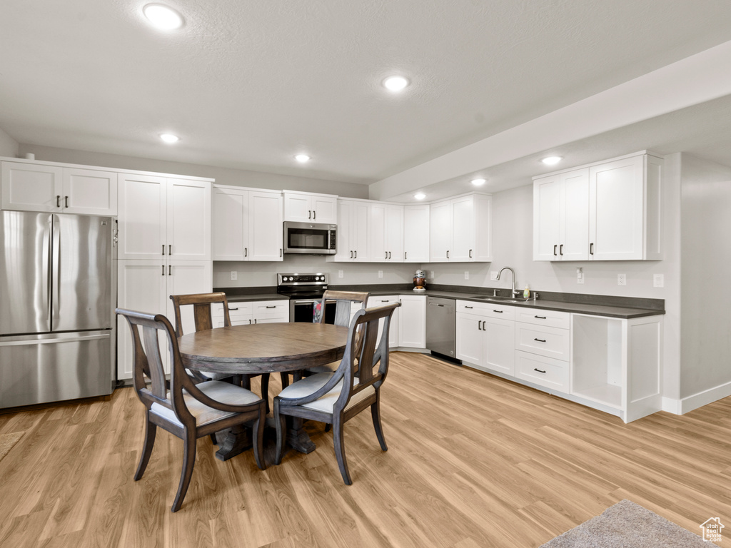 Kitchen featuring appliances with stainless steel finishes, recessed lighting, dark countertops, light wood finished floors, and white cabinetry
