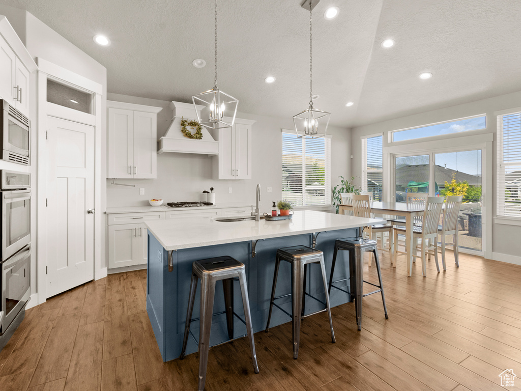 Kitchen with stainless steel microwave, a chandelier, premium range hood, light wood-style flooring, and gas cooktop