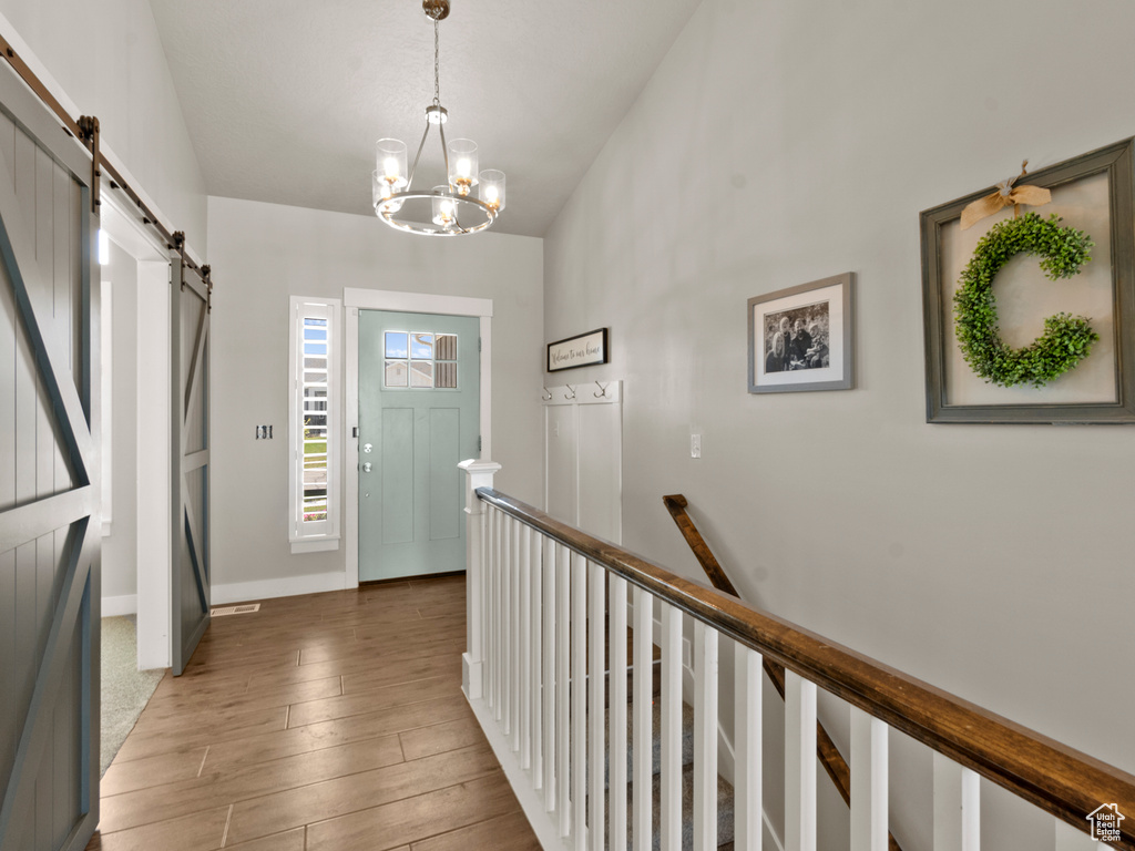 Foyer entrance featuring a barn door, wood finished floors, lofted ceiling, and a chandelier