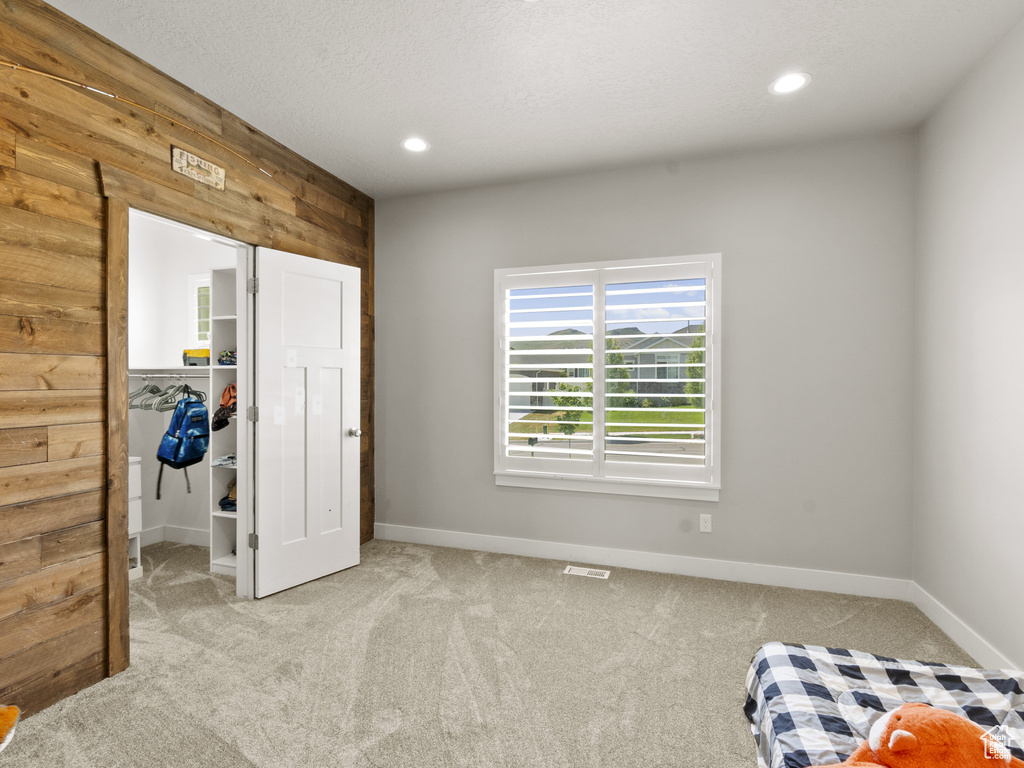 Bedroom featuring carpet floors, a spacious closet, recessed lighting, and wooden walls