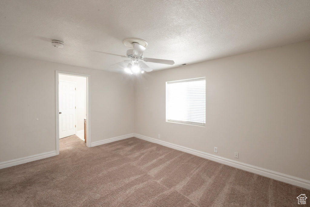 Spare room featuring a ceiling fan, light colored carpet, and a textured ceiling