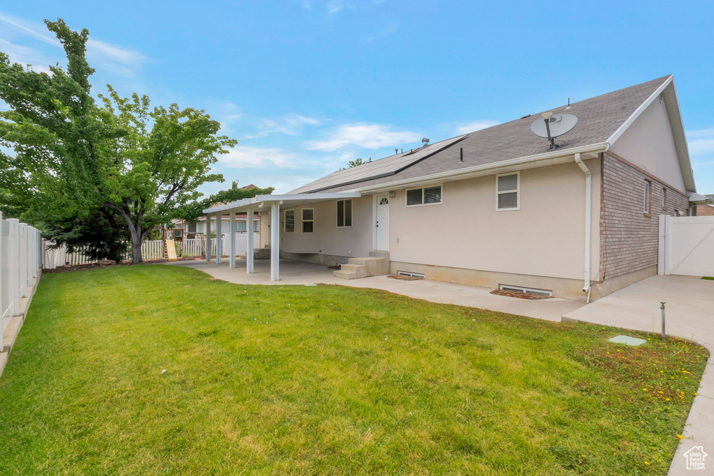 Rear view of house with a patio, a fenced backyard, roof mounted solar panels, and stucco siding