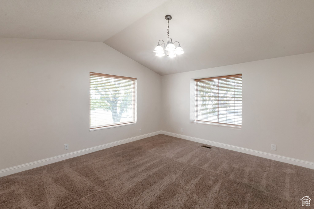 Carpeted spare room with a chandelier, plenty of natural light, and vaulted ceiling