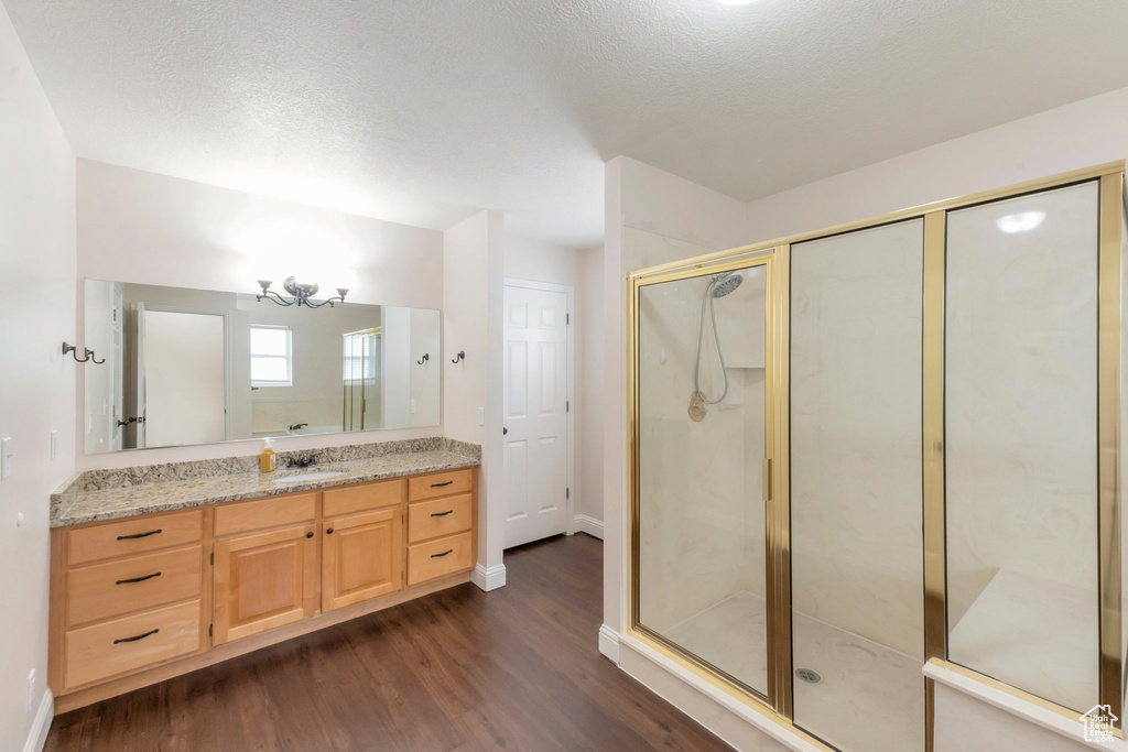 Full bathroom featuring wood finished floors, a shower stall, a chandelier, vanity, and a textured ceiling