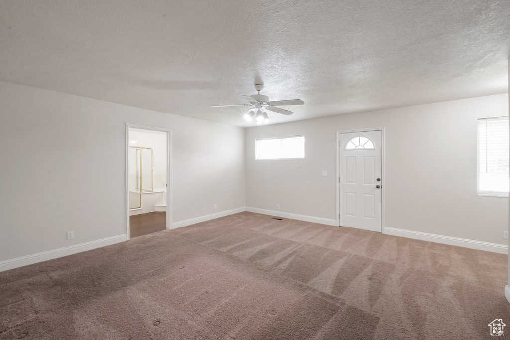 Entrance foyer featuring ceiling fan, light carpet, and a textured ceiling