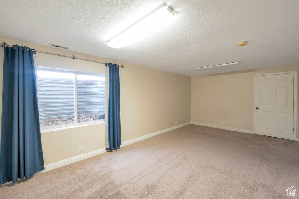 Carpeted empty room with a textured ceiling and a smoke detector