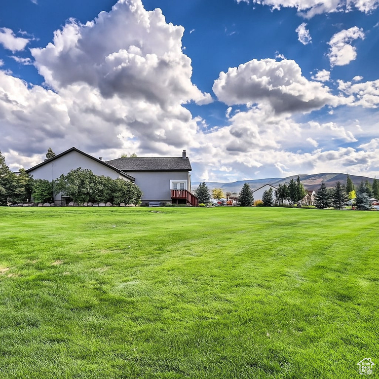 View of grassy yard with a deck with mountain view