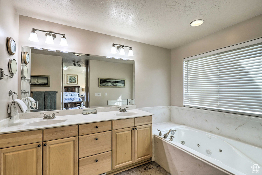 Full bath with a textured ceiling, ensuite bath, double vanity, and a tub with jets