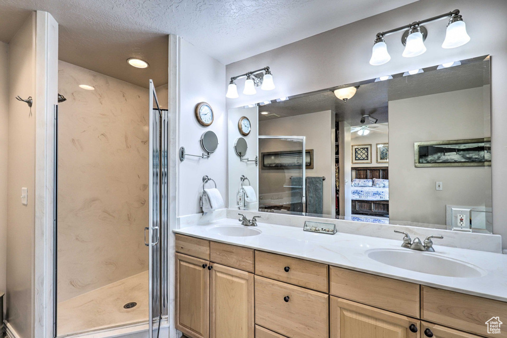Ensuite bathroom featuring double vanity, a stall shower, ceiling fan, and a textured ceiling