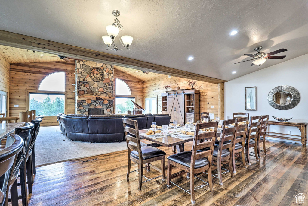 Dining room featuring lofted ceiling, wood walls, hardwood / wood-style floors, a chandelier, and ceiling fan