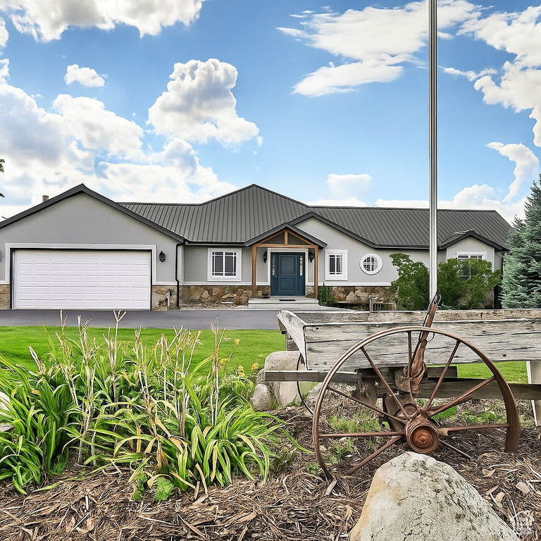 View of front facade featuring stone siding, a garage, asphalt driveway, a metal roof, and stucco siding