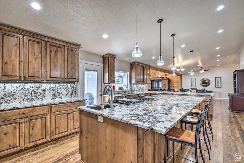 Kitchen with a kitchen island with sink, tasteful backsplash, recessed lighting, light wood-type flooring, and stainless steel gas cooktop