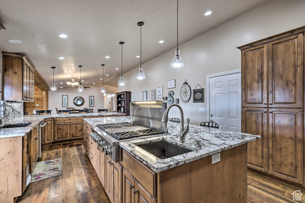 Kitchen featuring dark wood finished floors, a kitchen island with sink, recessed lighting, light stone countertops, and decorative light fixtures