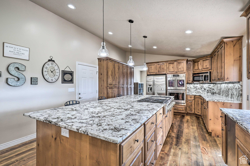 Kitchen featuring stainless steel appliances, lofted ceiling, brown cabinetry, a large island, and dark wood-style flooring
