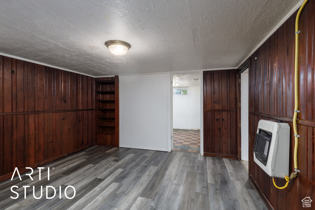 Unfurnished living room with heating unit, a textured ceiling, wood finished floors, and wooden walls