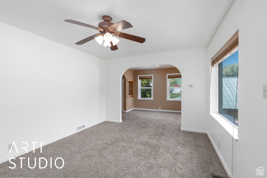 Carpeted spare room featuring arched walkways and a ceiling fan