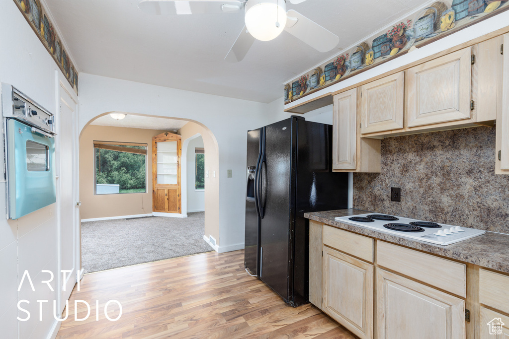Kitchen with white appliances, arched walkways, light brown cabinets, light wood-style flooring, and a ceiling fan