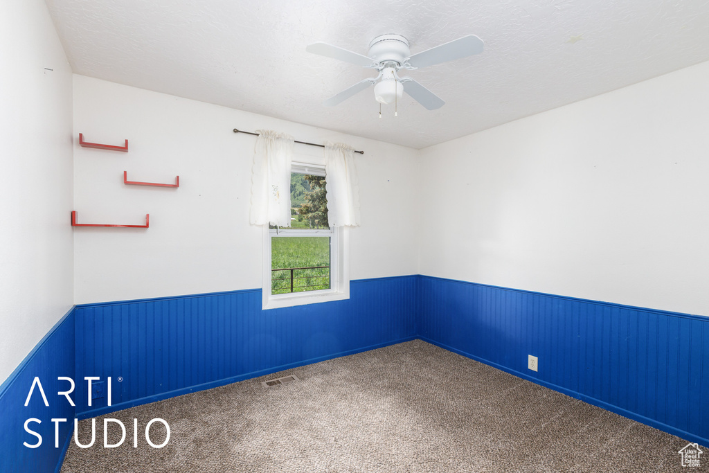 Unfurnished room with wainscoting, carpet floors, and a ceiling fan