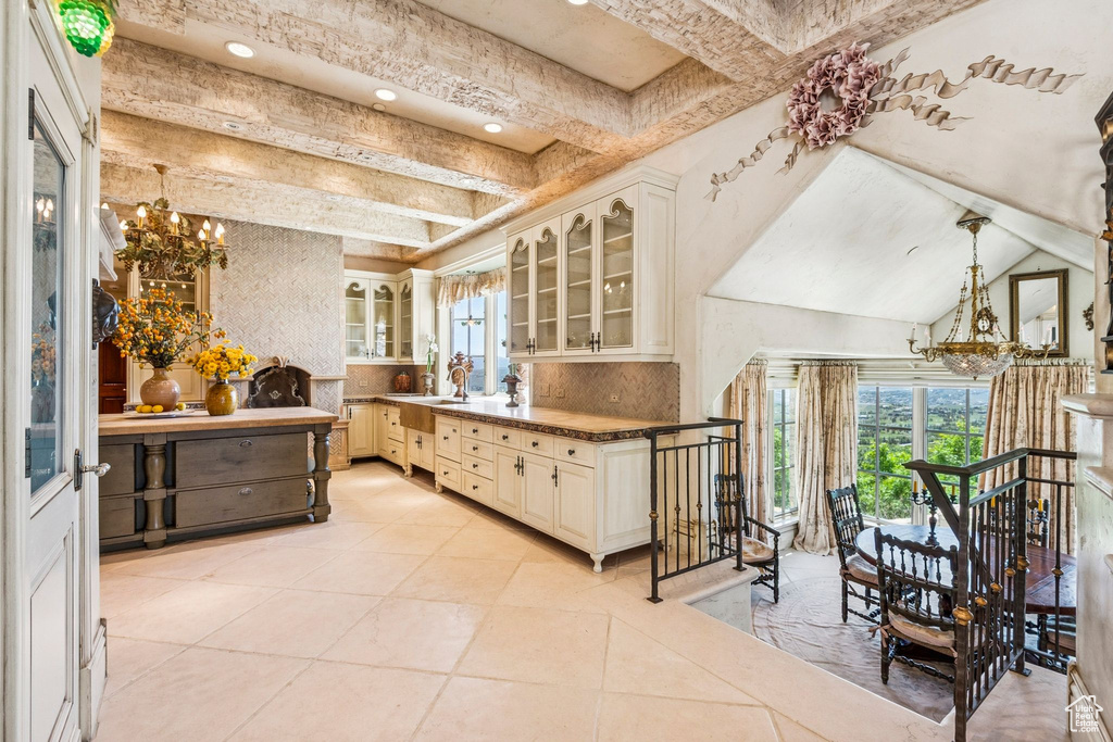 Kitchen with a chandelier, glass insert cabinets, beam ceiling, backsplash, and light tile patterned floors