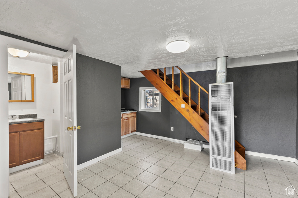 Below grade area with a heating unit, stairs, a textured ceiling, and light tile patterned floors