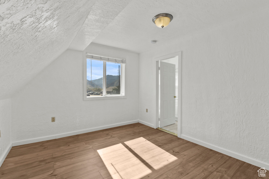 Additional living space featuring a textured ceiling, wood finished floors, and vaulted ceiling